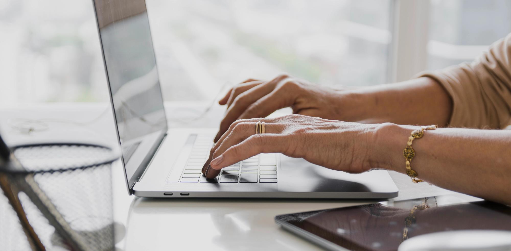 Hands typing a follow-up email after meeting on a laptop, drafting next steps and action items in a post-meeting recap email.