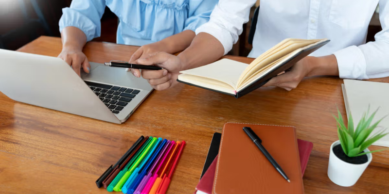 Teachers collaborating on laptop using a school administration software setup at a shared workspace.